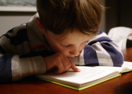 Kind, das ganz konzentriert ein Buch liest, das auf einem Tisch liegt